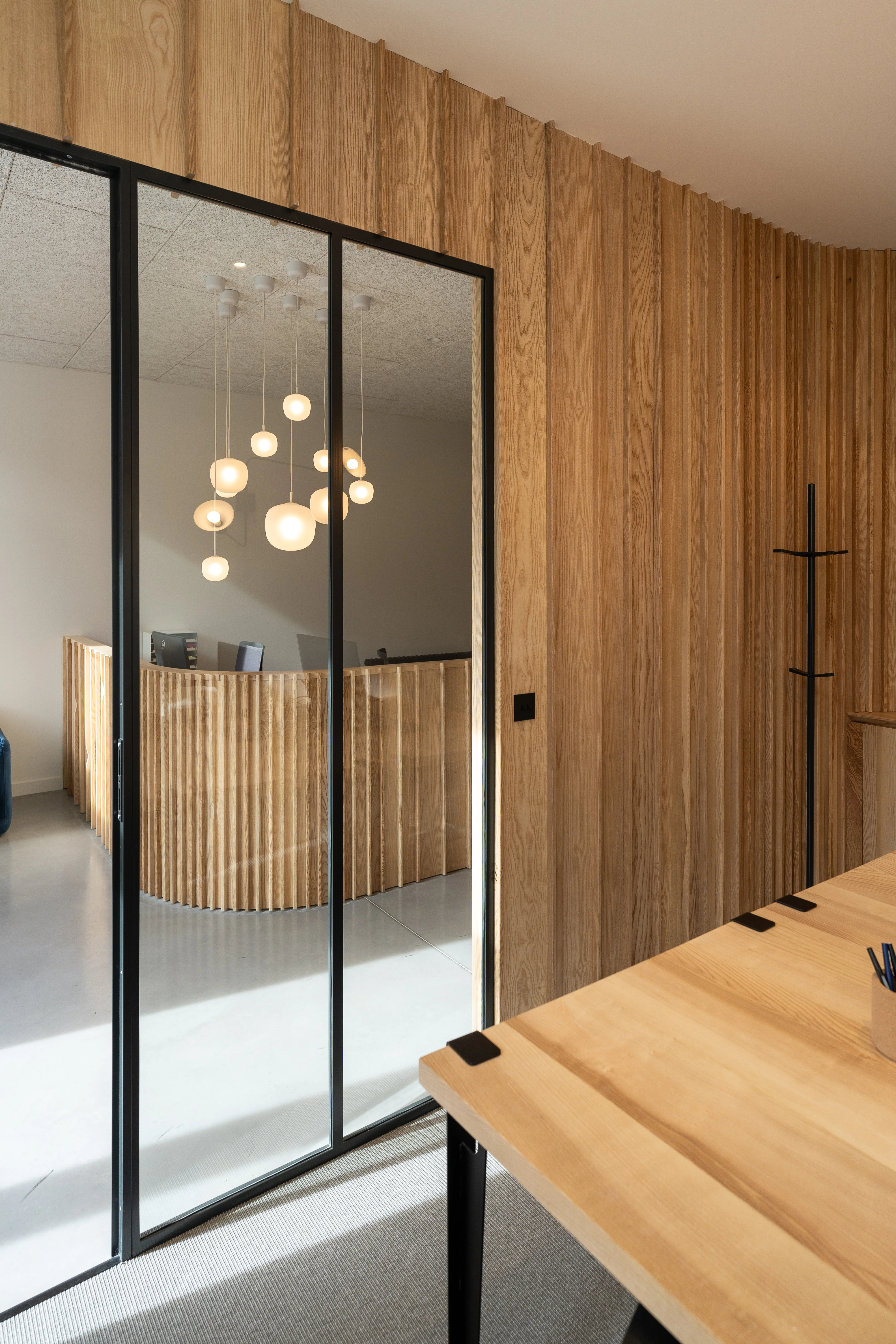 Vue depuis l'espace de travail sur la cloison courbe en frêne massif d'Isère et la verrière acier, projet Au Bonheur des Dames, Saint-Martin-d'Uriage. Atelier Joëlle Personnaz architecte. Photo A. Frénot.