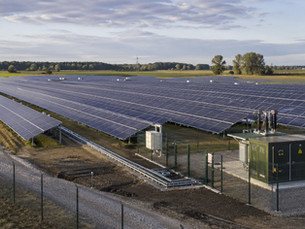 Photorealistische Aufnahme eines großen Solarparks in einer ländlichen Landschaft in Deutschland mit langen Reihen von Solarmodulen, einem Transformator und sichtbarer Netzinfrastruktur im Vordergrund.