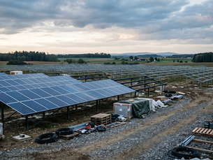 Teilweise fertiggestellter Solarpark auf einer Baustelle mit installierten und noch fehlenden PV-Modulen unter leicht bewölktem Himmel, der eine verzögerte Inbetriebnahme symbolisiert.