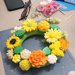 Bright yellow and orange wax melt flower wreath on crafting table during DIY workshop in Athens.