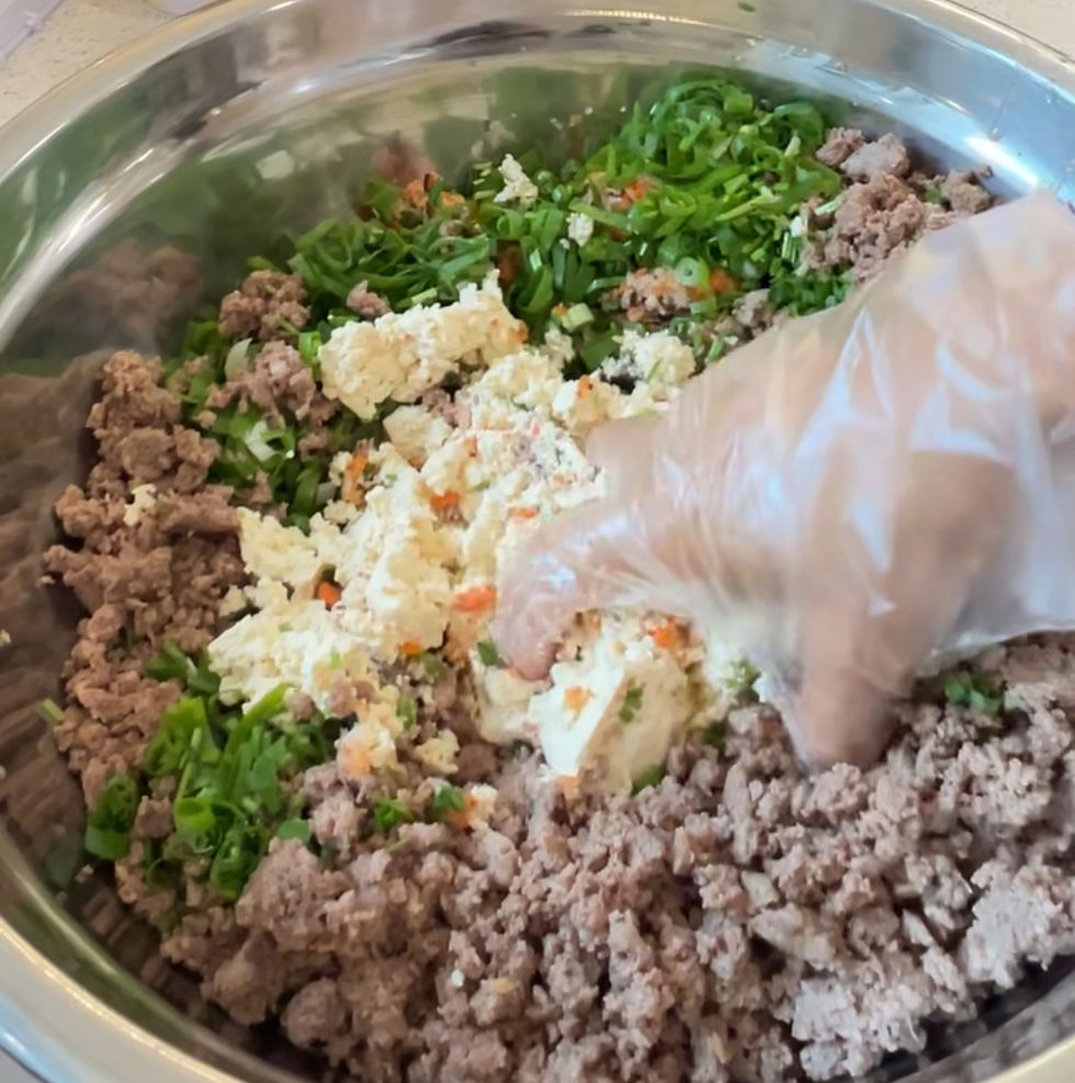 볼에 다진 고기, 잘게 썬 채소, 비닐장갑을 낀 손이 재료를 섞는 중입니다. 음식 준비 과정입니다.