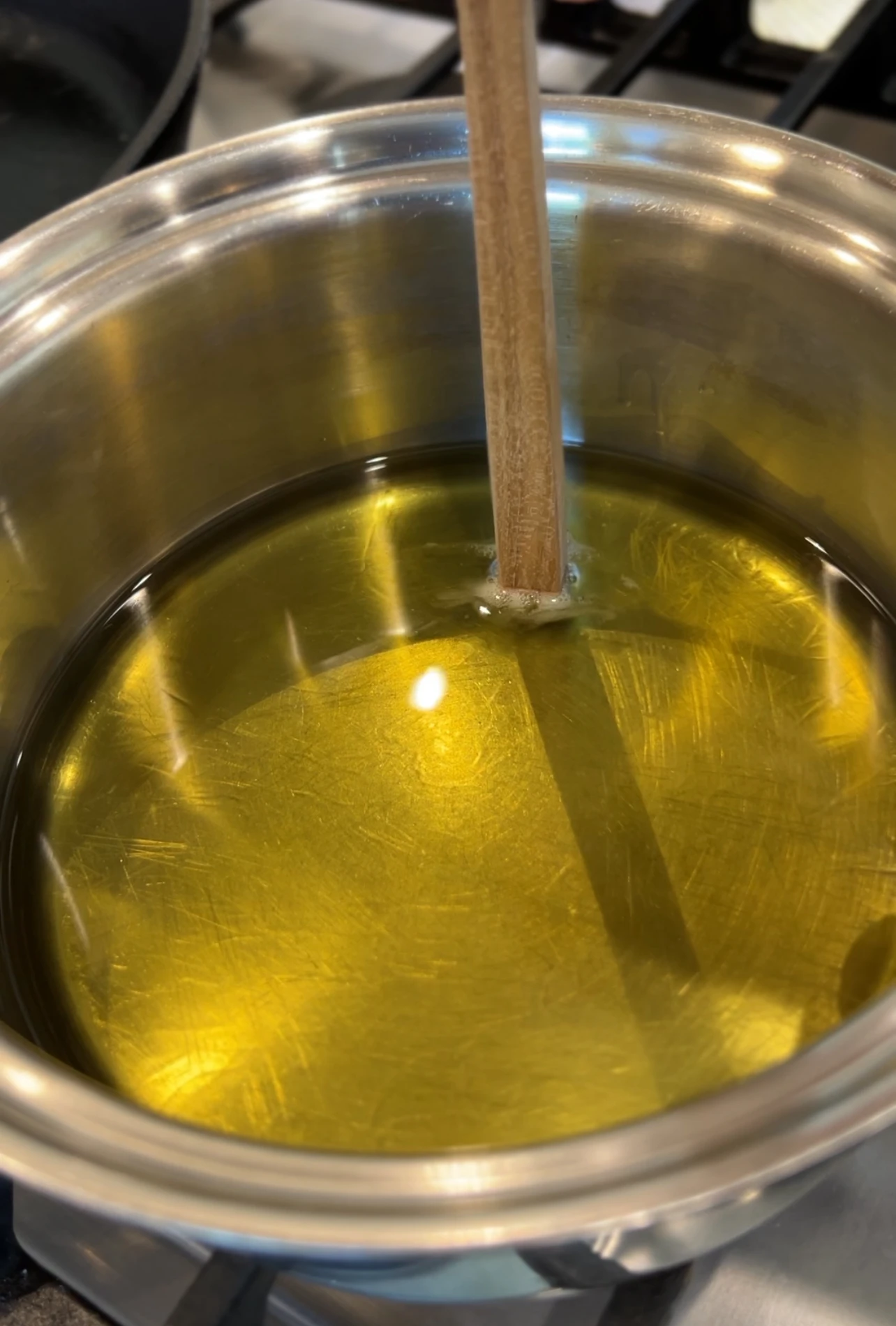 스텐솥 안에 기름에 나무스틱을 찔러넣어 있는 상태. 나무스틱에 기름이 접촉되는 부분에 버블이 일어나고 있다.