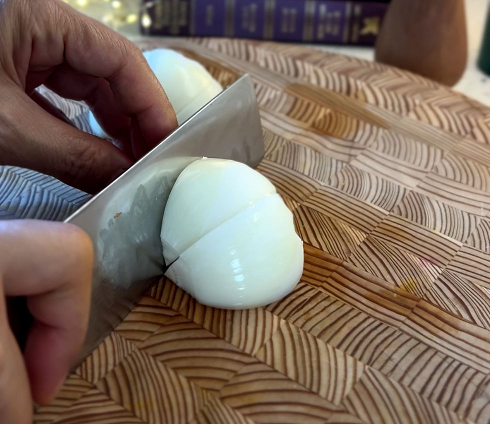 나무 도마 위에 양파가 놓여 있고, 손이 칼로 이를 자르는 동작을 하고 있다. 도마의 나뭇결 패턴이 뚜렷하다.