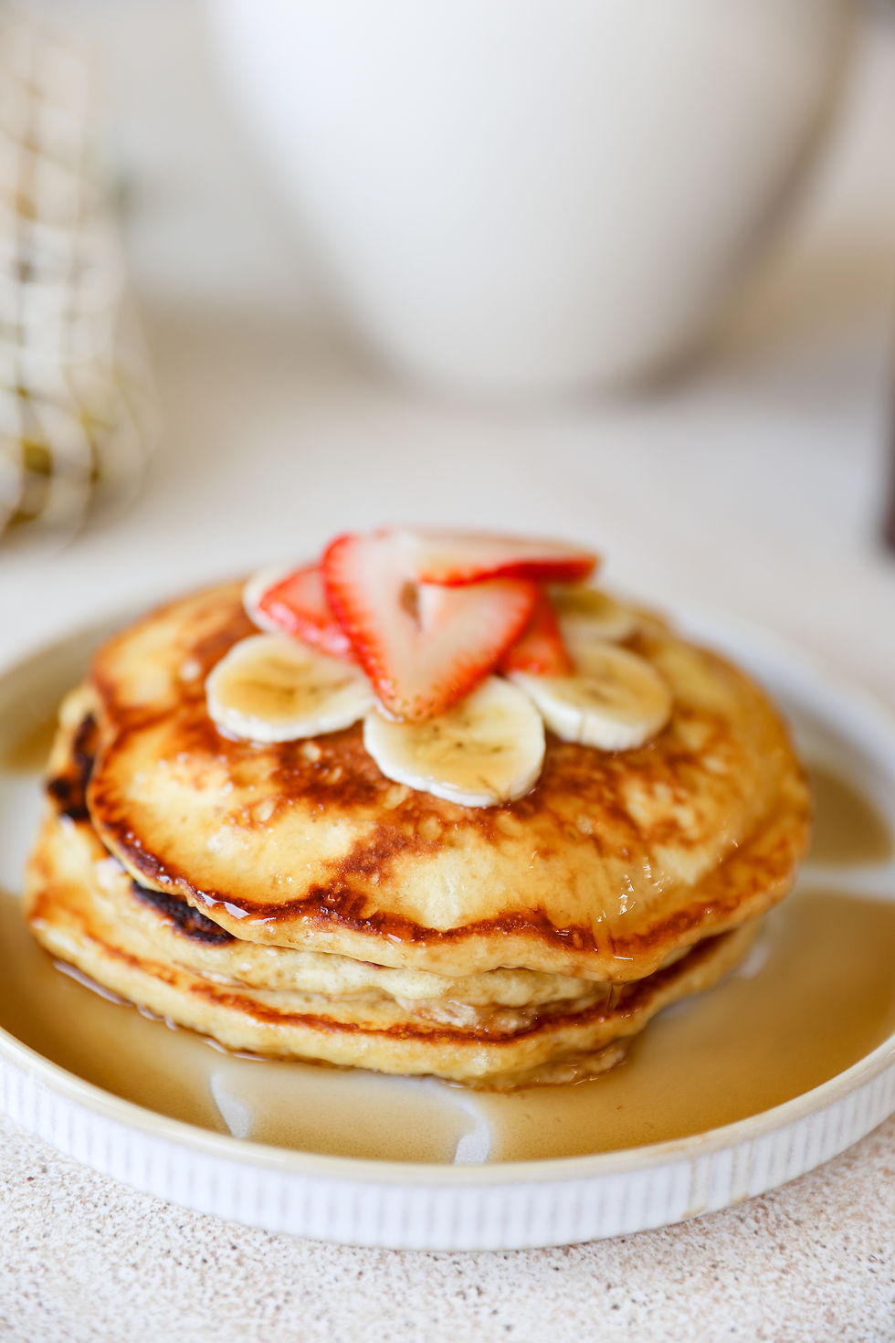 Homemade fluffy pancakes topped with maple syrup, fresh strawberries, and sliced banana in natural light