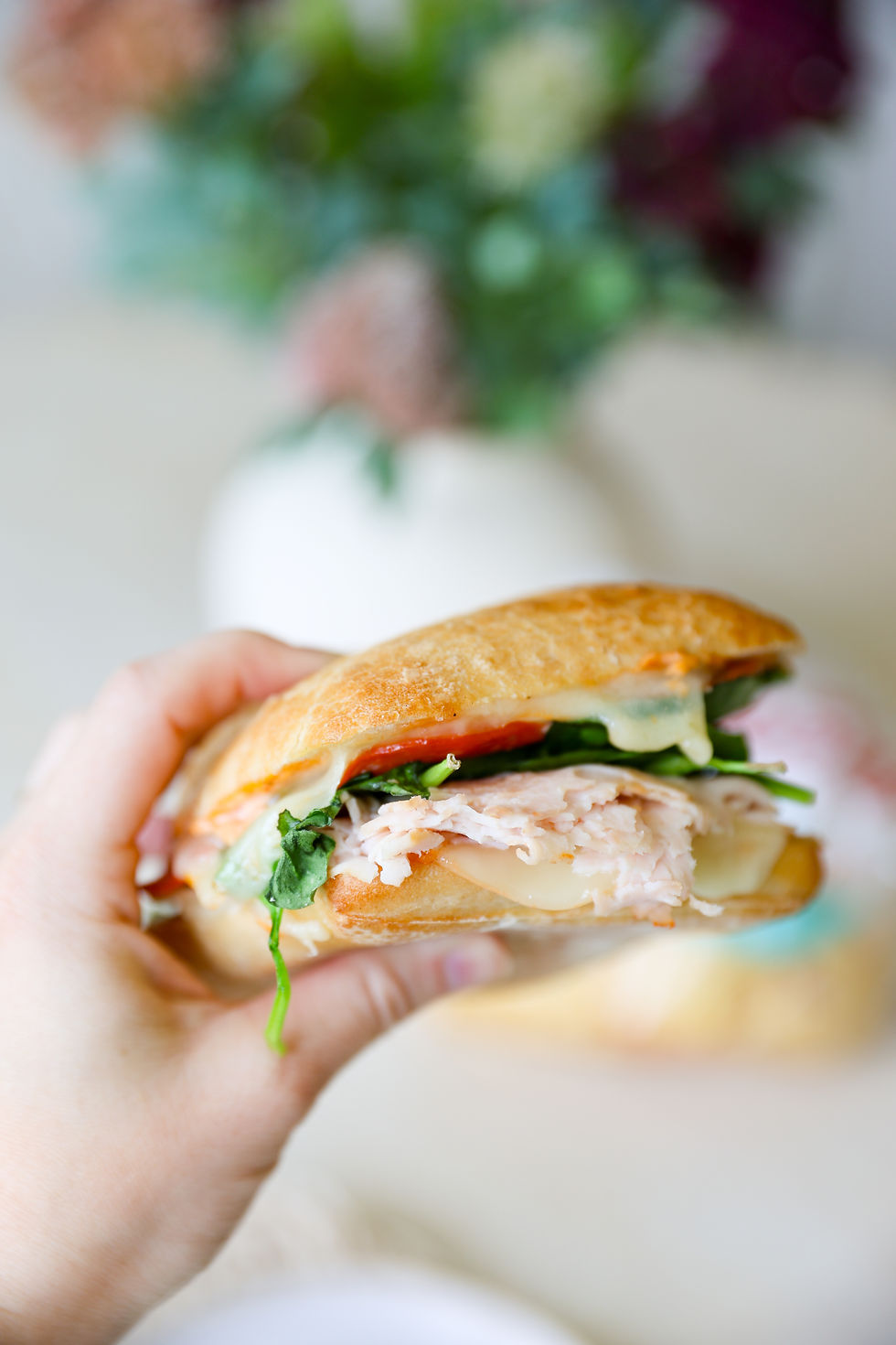 Toasted ciabatta sandwich filled with turkey, pepperoni, provolone, swiss cheese, spinach, and creamy homemade smoky mayo sauce on a wooden board.