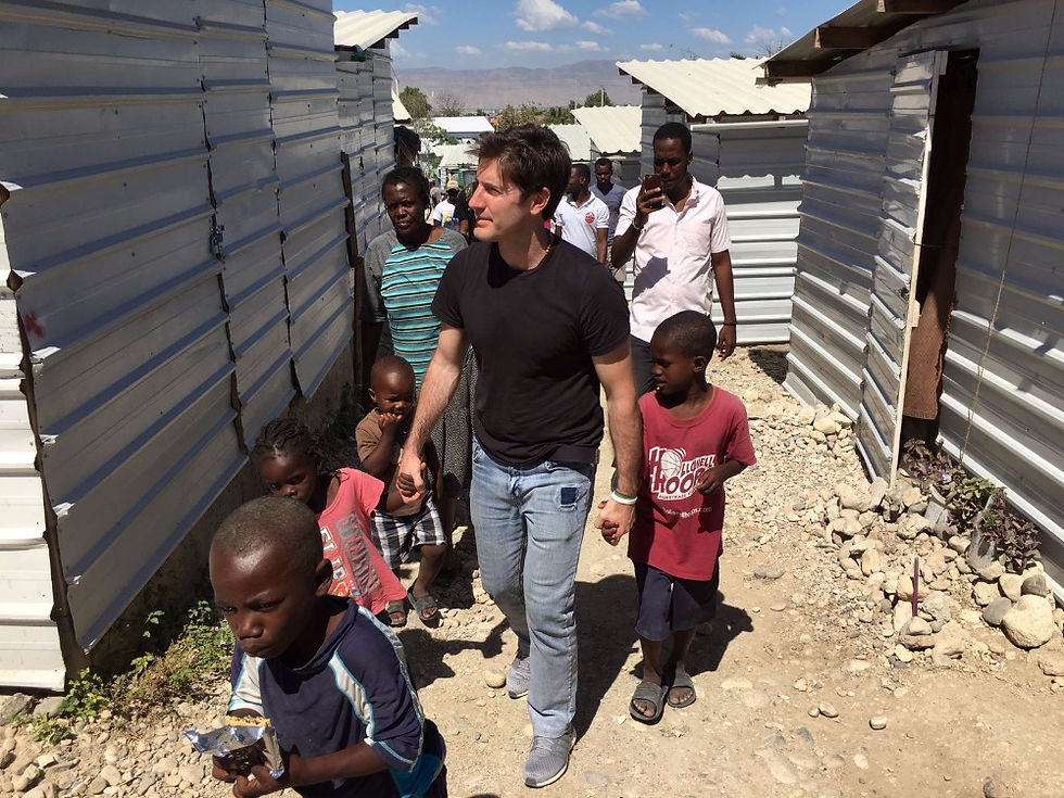 Nicolás García Mayor walking hand-in-hand with children through a modest, displaced community area, reflecting his humanitarian mission through CMAX shelters.