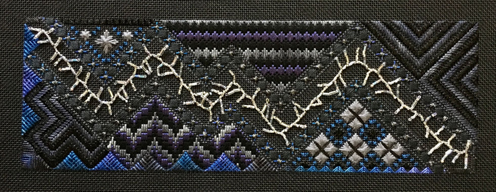 Geometric needlepoint design on black background with black, dark gray, dark blue, and dark purple threads. Shiny silver beads make a zig zag line like lightning across the center of the piece.