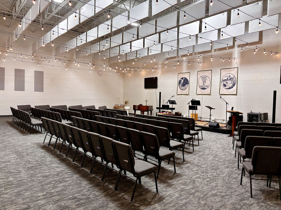 A view of the sanctuary from the right back by the entryway. An open isle with four sections of chair rows.