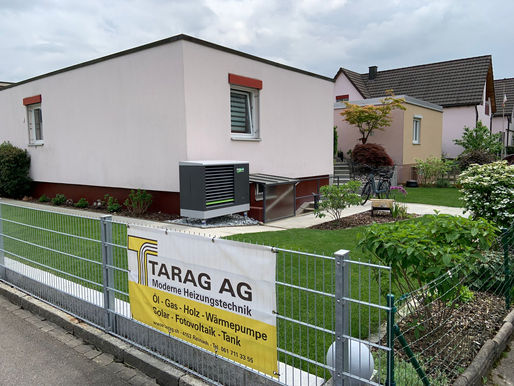 Referenzobjekt der Tarag: Einfamilienhaus mit Wärmepumpe im Garten. Davor ein Zaun mit einer Tarag Werbeblache.