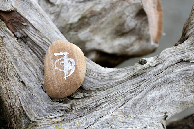 A close up image of a healing reiki symbol drawn on a smooth stone and resting on a weathe