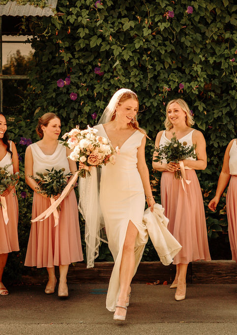 Napa Valley bride in modern white wedding dress walking with bridesmaids in blush dresses holding bouquets at Tre Posti wedding