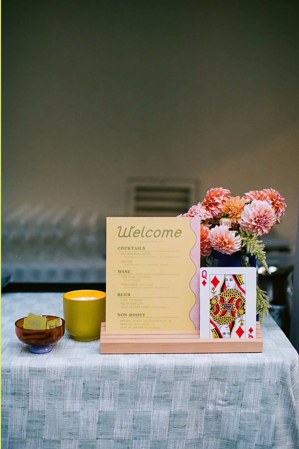 wedding welcome party table with cocktail menu signage, candle, and floral arrangement