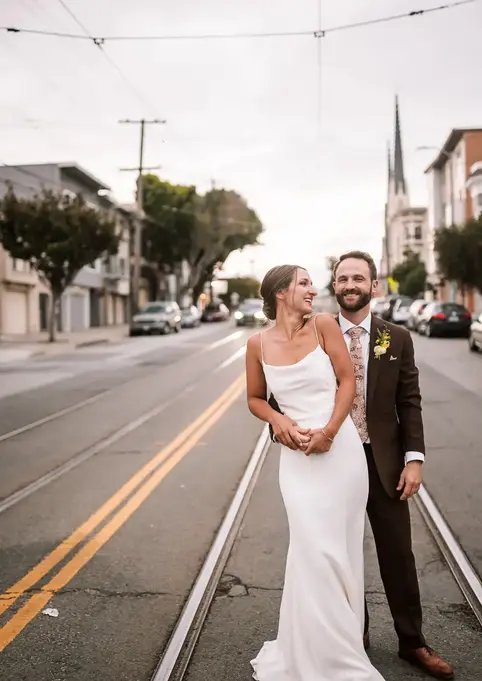 A couple in wedding attire embracing on a city street with tram tracks.