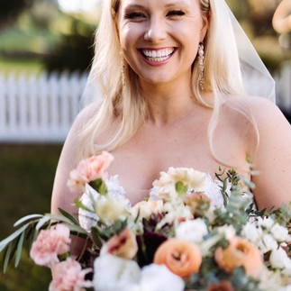 Smiling bride holding a bouquet of flowers outdoors.