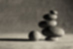 Smooth stones stacked on a sandy surface, with one stone beside. Monochrome background suggesting the calm, balanced mood we need when we engage with our spiritual shadow.