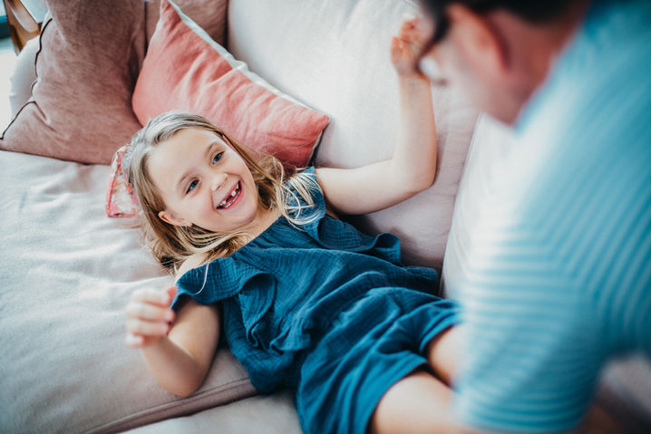 Smiling girl on couch with parent for family home photo shoot