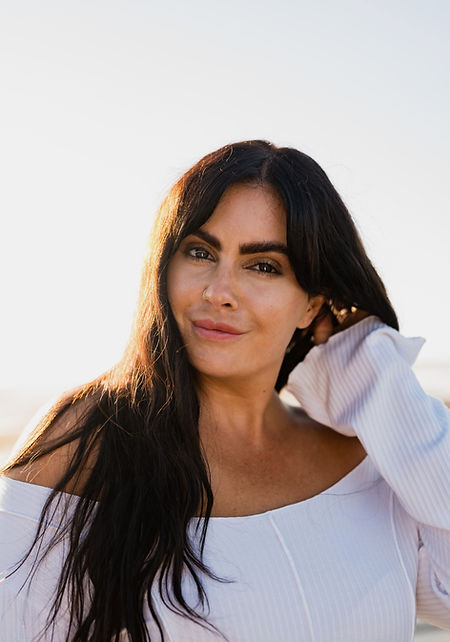 Stress Coach Steph Williams, The Rested Woman, facing the camera for a headshot with her hand running through her long hair and a dimpled smile on her face with sparkling bright eyes and stylised eyebrows.