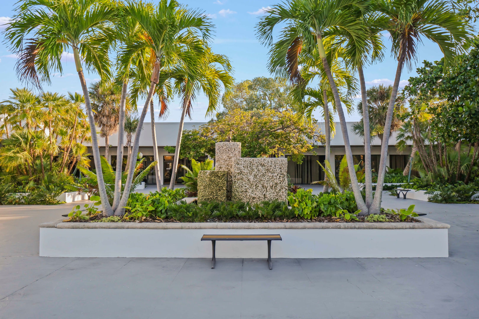Palm trees, stone planter, and bench at shopping center entrance.