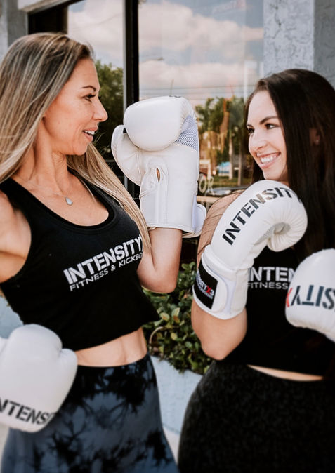 Two women smiling, wearing 'INTENSITY' boxing gloves