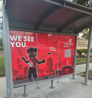 A bright, red bus shelter featuring the UC Bearcat mascot and text that reads "We See You."