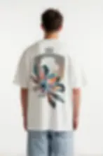 Model wearing KENDZ men’s oversized white t-shirt with crest and floral back print - streetwear style