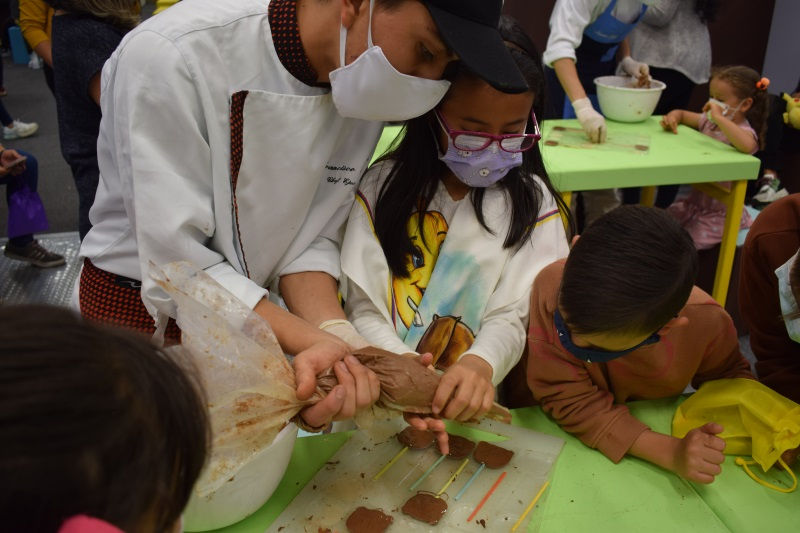 Un artesano de chocolate le enseña a niños el proceso para usar una manga pastelera con chocolate