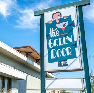 Sign reading "The Green Door" with an image of a cartoon man peering over the edge and a Martini next to the text