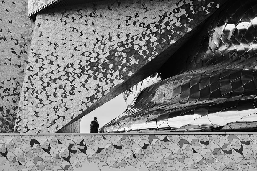 Détail de façade de la Philharmonie de Paris avec une silhouette humaine à proximité