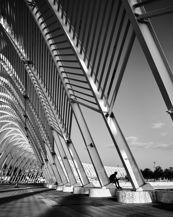 Photographie fine art Athènes – silhouette parmi arches métalliques répétitives, lumière naturelle et minimalisme.