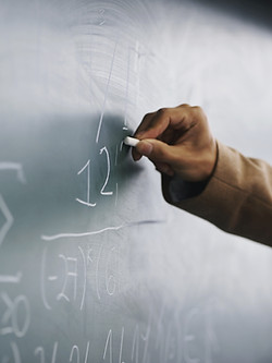 Teacher Writing a Formula on a Blackboard