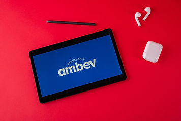 Laptop preto exibindo o logo da empresa Ambev e com um fundo vermelho