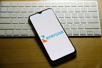 Smartphone apresentando o logo da empresa Energisa. Ao fundo, teclado branco de laptop
