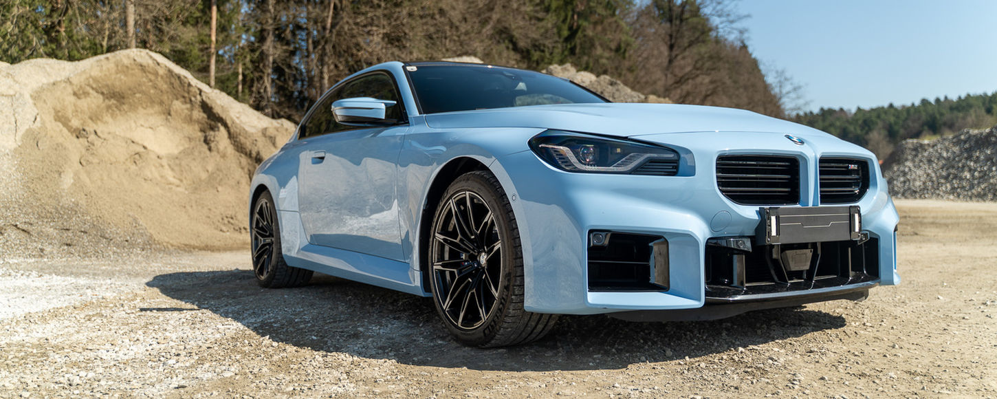 BMW M2 in Seitenansicht vor einem großen Kieshaufen