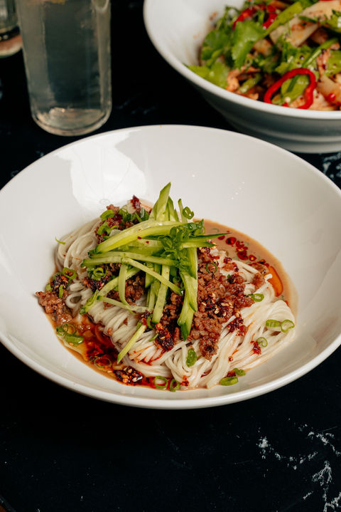 Dan Dan sesame noodles topped with ground pork, roasted sesame, Sichuan chili crunch, and fresh cucumber — a bold, aromatic signature from QUA Contemporary Chinese Cuisine.