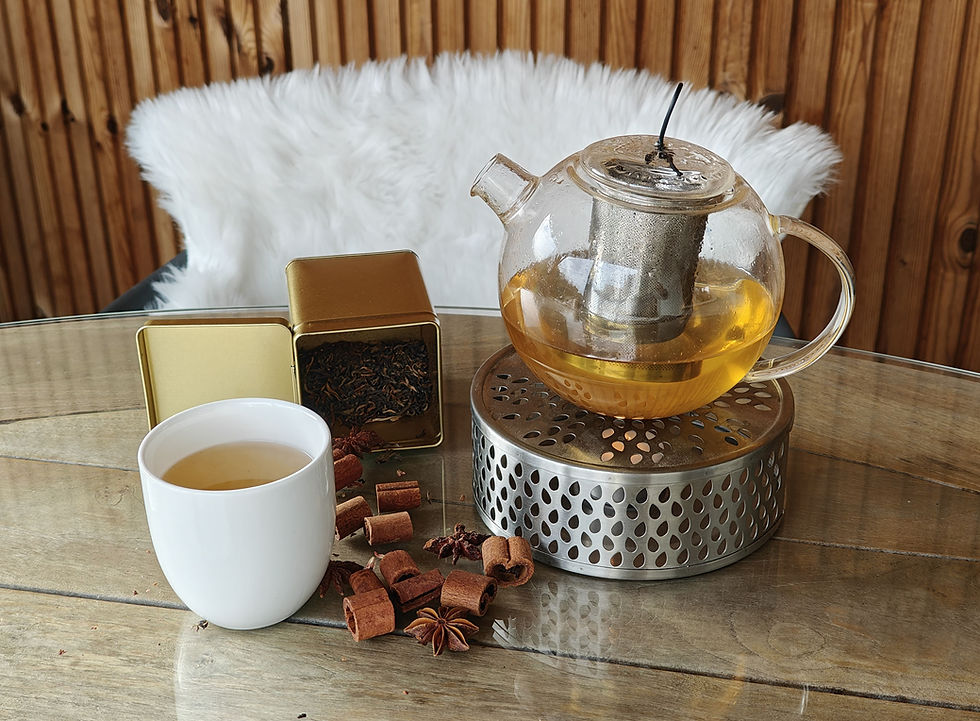 Thé d’hiver Goûthee dans une théière en verre posée sur un chauffe-théière, accompagné d’une tasse blanche et de bâtons de cannelle.