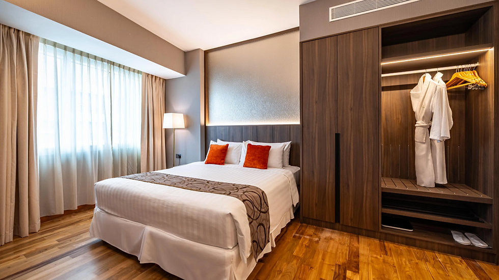 Modern hotel bedroom by TCG Construction with a neatly made bed, orange pillows, floor lamp, and open wardrobe holding white robes.