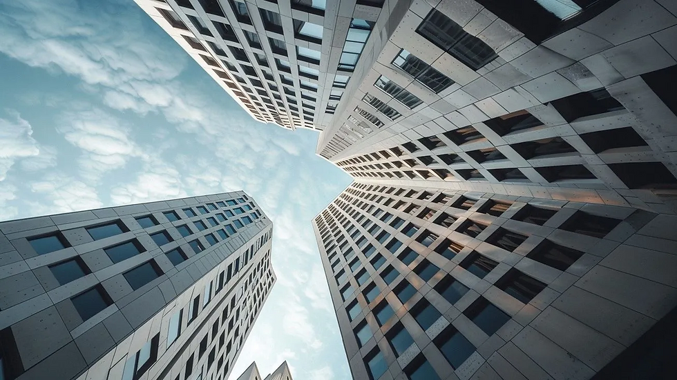 Looking up between four modern skyscrapers with geometric windows against a blue, clouded sky.