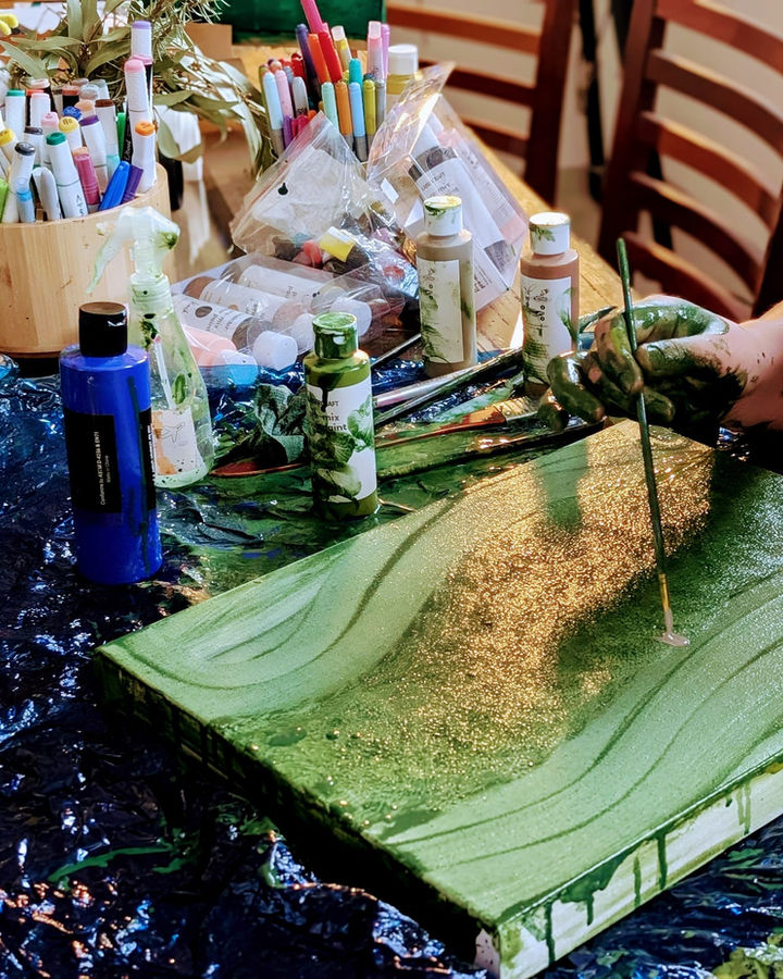 Paint-covered hands working on a green and gold canvas