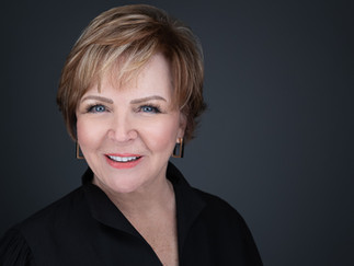 Professional headshot of a woman with short hair wearing a black top with polished styling and soft studio lighting