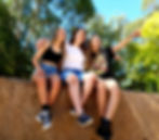 Three teenage girls are sitting on a wall laughing.
