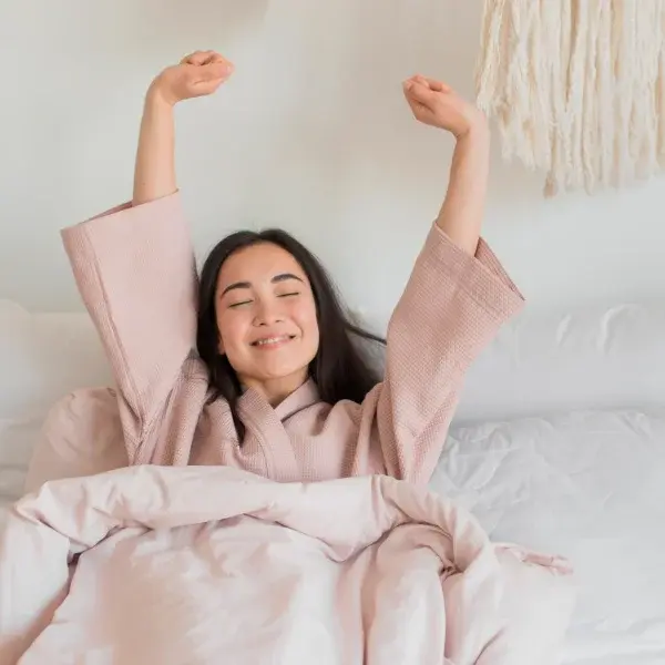 A woman in a pink robe relaxes in bed, preparing for a stress reduction massage.