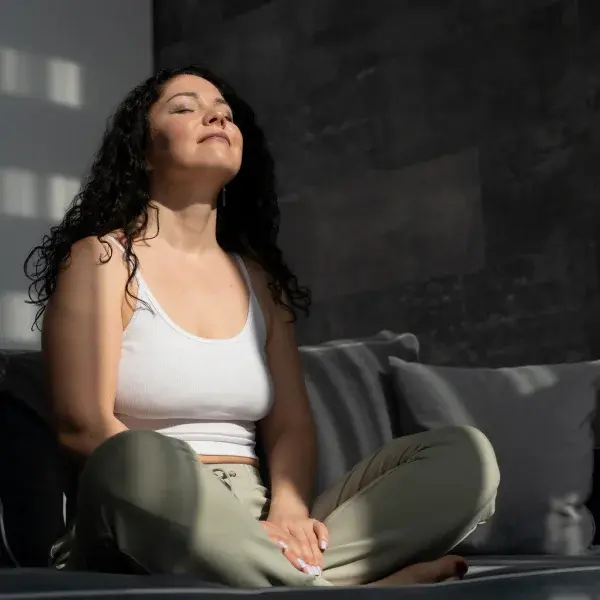 A woman sitting on a couch with her eyes closed, enjoying relaxation, highlighting the benefits of massotherapy.