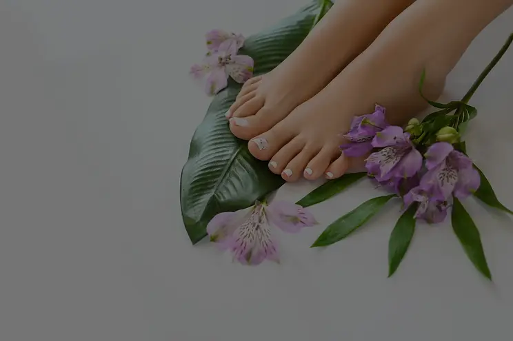 A close-up of female feet adorned with flowers and green leaves, set against a clean white background, showcasing a pedicure.