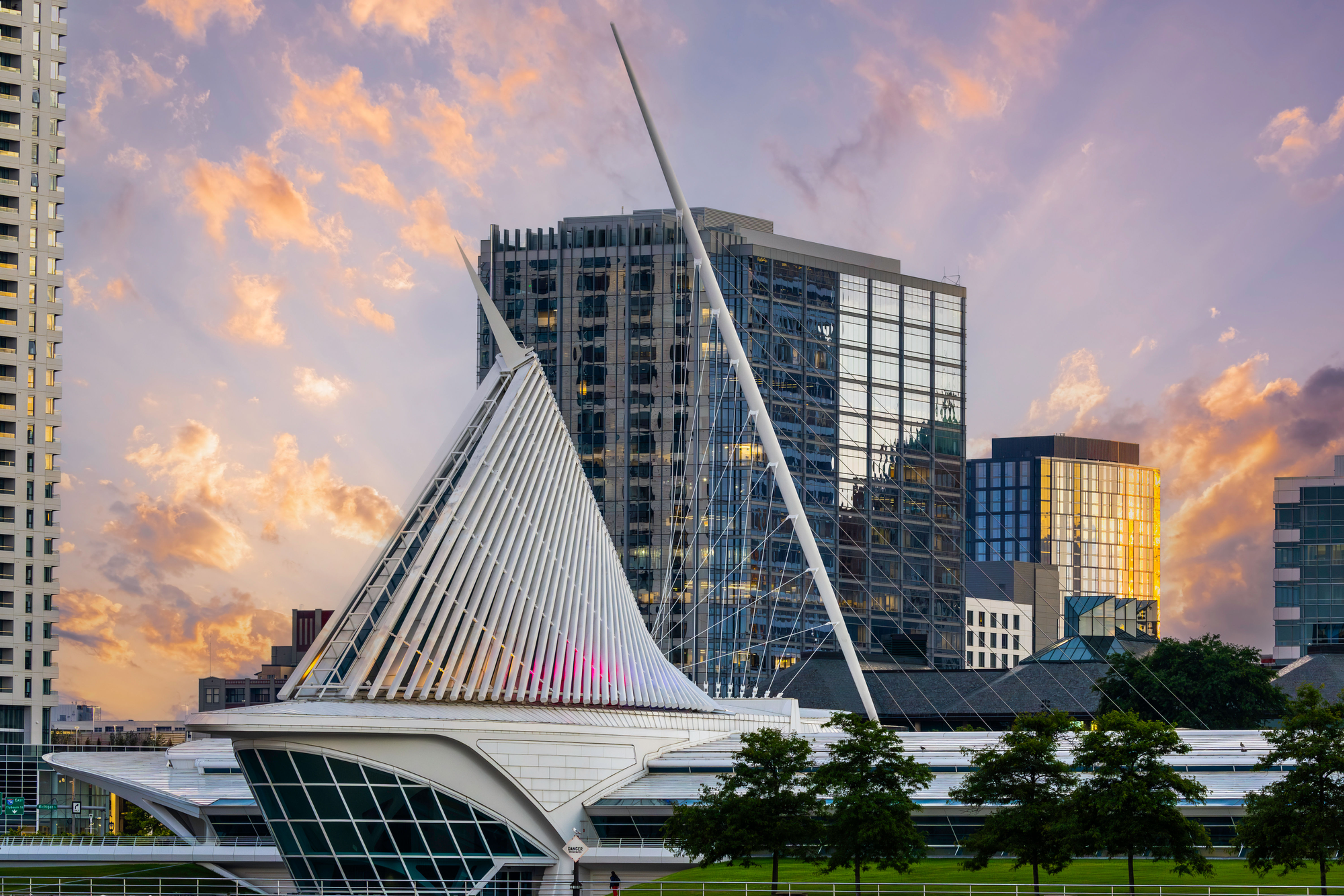 Architectural photograph of the Milwaukee Art Museum at sunset, showcasing its sail-like structure with surrounding skyscrape
