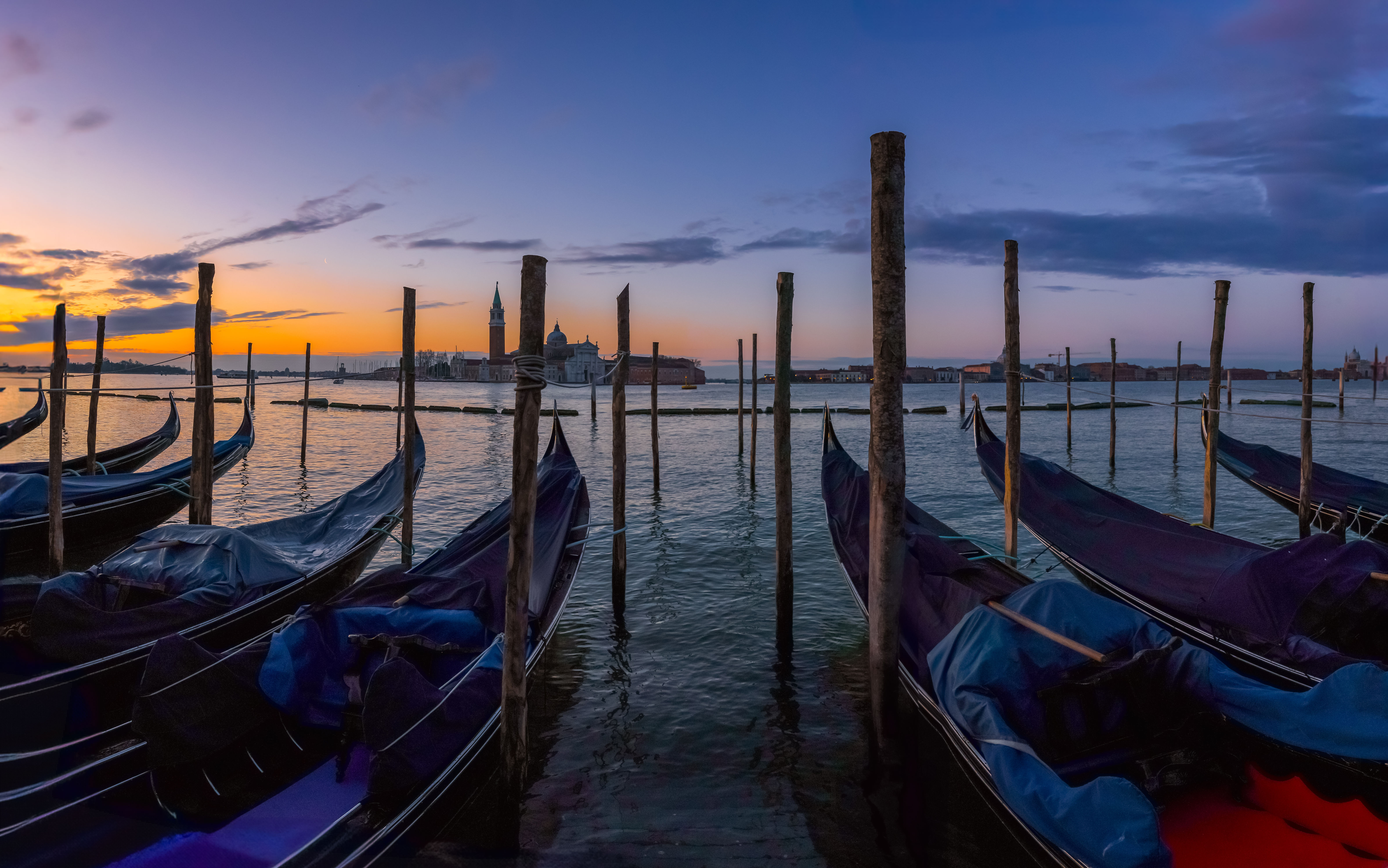 Twilight view of gondolas docked in Venice, Italy with the silhouette of San Giorgio Maggiore island and a vibrant sunset sky