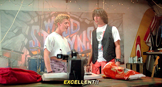 Gif of Bill and Ted from Bill and Ted's Excellent adventure . they're playing air guitar and saying "excellent"