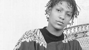 Black and White picture of a young woman (Liz Obi). Her is in twists and frames her face and her background is patterned background. 