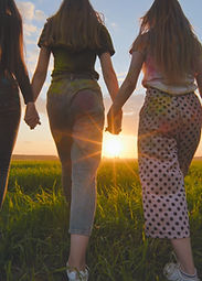 A group of girls walk towards the sun at sunset holding hands.jpg