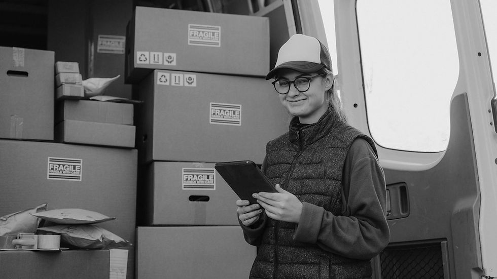 A delivery woman holding a tablet stands next to van full of parcels.