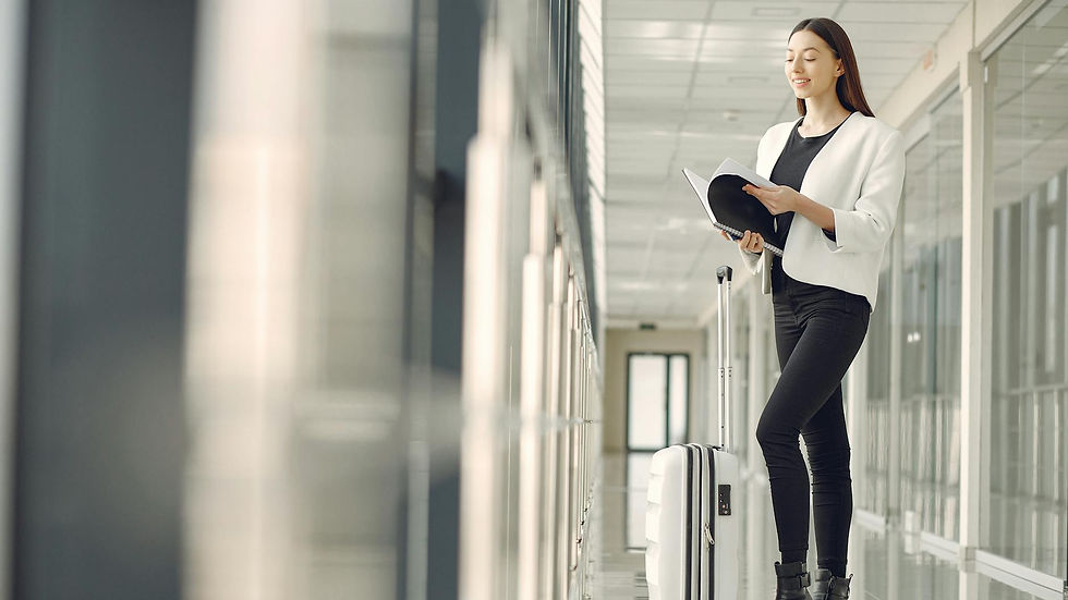 Full body of slim female businesswoman in formal clothes with suitcase standing in airport hallway and reading note in notebook while waiting for flight